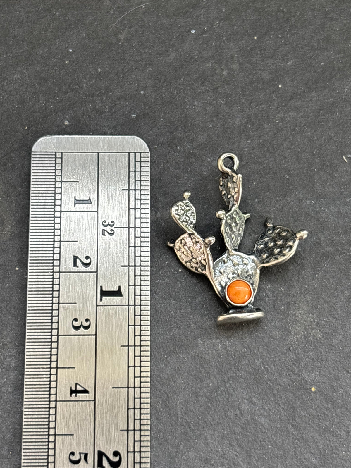 Orange Spiny Oyster Prickly Pear Cactus Charm in sterling silver, beside a vertical ruler for scale