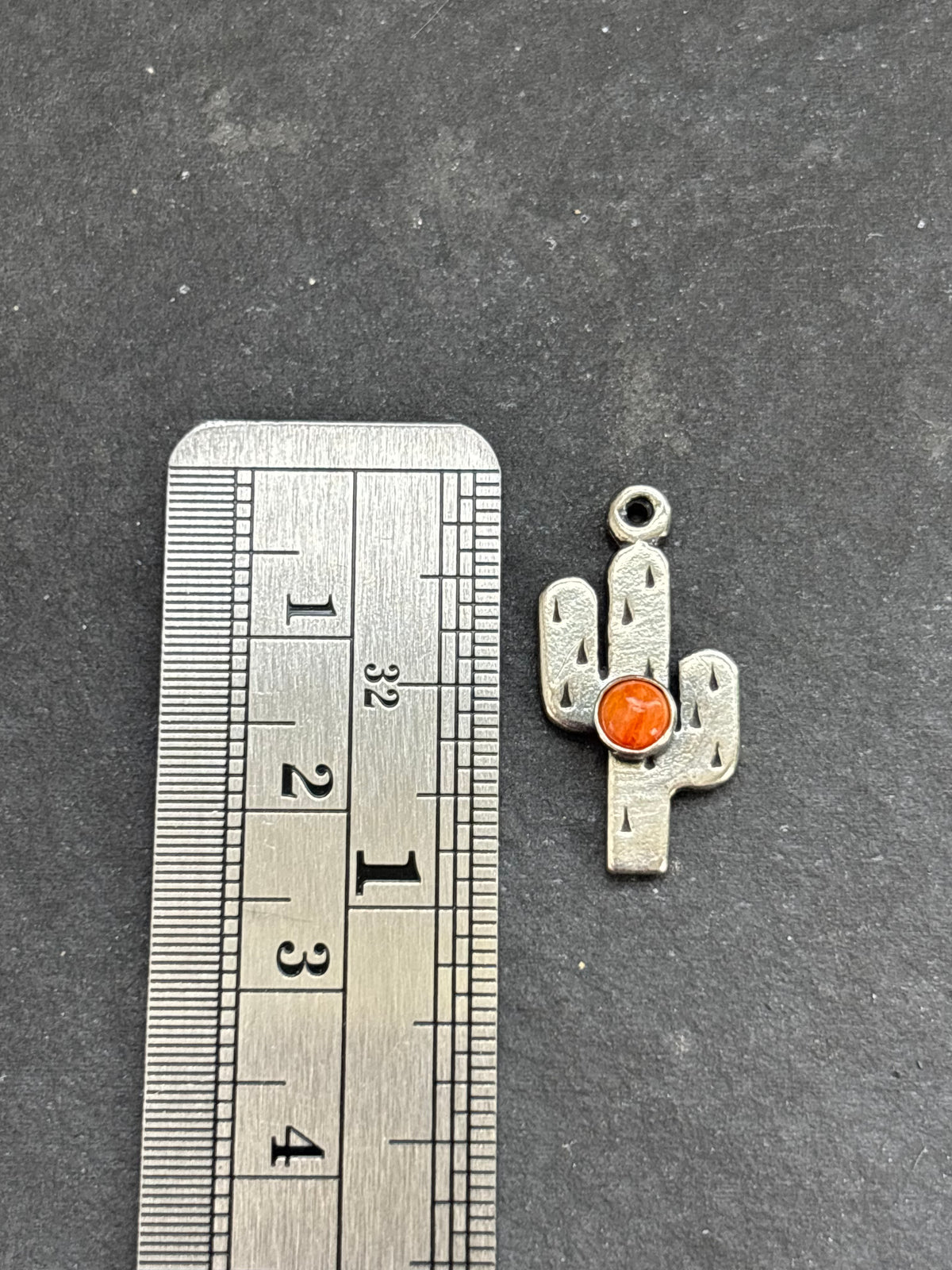 Orange Spiny Oyster Saguaro Cactus Charm in sterling silver, beside a vertical ruler for scale